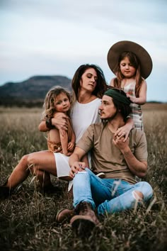 a family sitting in the grass with one child on his shoulders and two other children standing behind them