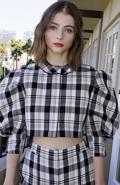 a woman standing in front of a door wearing a black and white checkered shirt