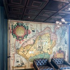 a map is on the wall behind two leather chairs