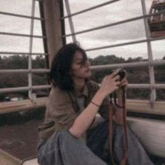 a woman sitting on the side of a train holding a camera up to her face