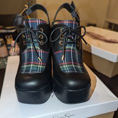 a pair of black shoes with plaid linings on top of a white box in a room