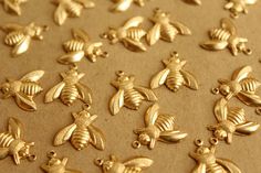 many gold bee charms are shown on a sheet of brown paper with black dots around them