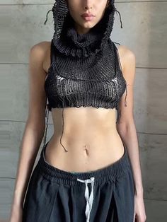 a woman wearing a black top and skirt with chains on her head is standing in front of a wall