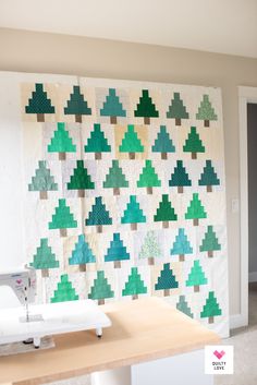 a quilted christmas tree wall hanging next to a sewing machine on a counter top