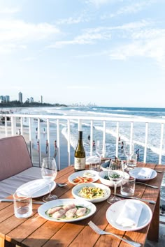 a wooden table topped with plates of food next to the ocean