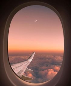 an airplane window with the view of clouds and a crescent in the sky at sunset