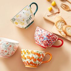 three colorful cups sitting on top of a table next to some bread and lemons