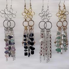 four pairs of earrings hanging from chains on a white background, with beads and rings attached to them