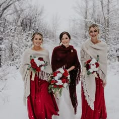 three bridesmaids in red dresses and shawls standing in the snow