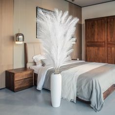 a white vase filled with feathers on top of a bed next to a night stand