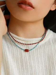 a close up of a person wearing a white sweater and necklace with red beads on it