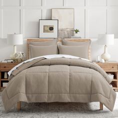 a bed with beige comforter and pillows in a white room next to a dresser