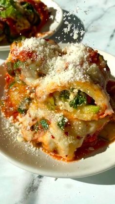 two white plates topped with lasagna covered in parmesan cheese and broccoli