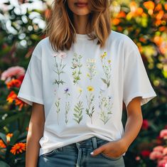 a woman standing in front of flowers wearing a white t - shirt with wildflowers on it