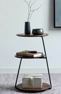 two tiered tables with books and vases on them in front of a white wall