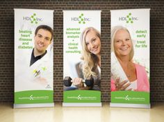 three roll up banners on the side of a brick wall with two smiling people behind them