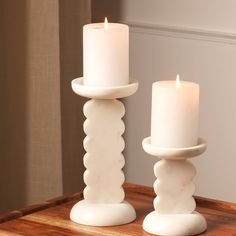 two white candles sitting on top of a wooden table