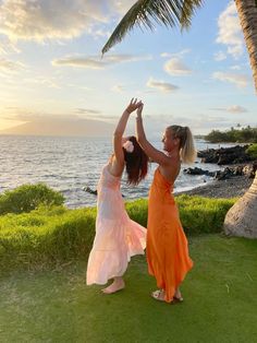 two women in orange dresses reaching up into the air