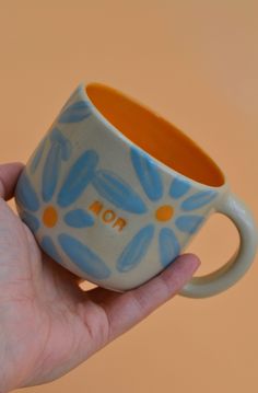 a hand holding a blue and orange coffee cup