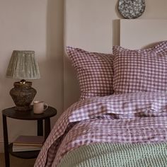 a bed with purple and green checkered comforter next to a table with a lamp on it