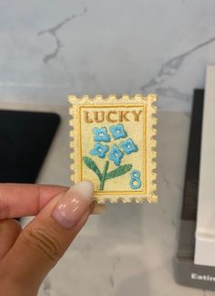 a person holding up a small stamp with flowers on it and the word lucky written in blue