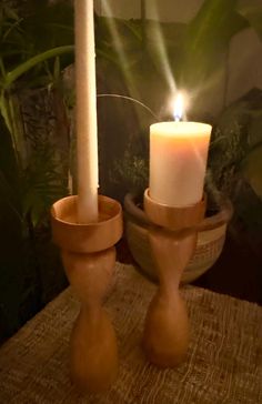 two candles sitting on top of a table next to a potted plant in the background