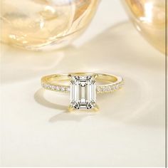 an emerald - cut diamond engagement ring sits next to champagne glasses