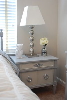 a nightstand with a lamp on top of it next to a white flower vase and an owl figurine