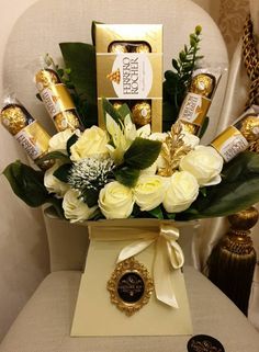 a vase filled with white flowers sitting on top of a chair next to some chocolates