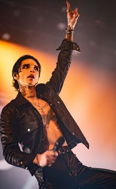 a man with tattoos on his chest holding a microphone and wearing a black leather jacket