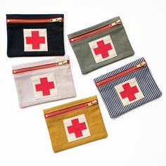 four small zippered pouches with red crosses on the front and sides, all lined up in different colors