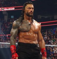 a man with long hair and tattoos standing in front of a crowd wearing red boxing gloves