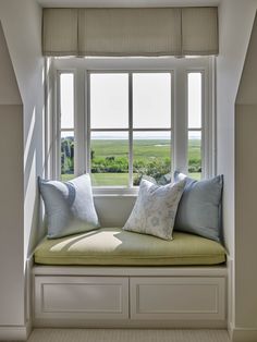 a window seat with pillows on it in front of a window overlooking an open field