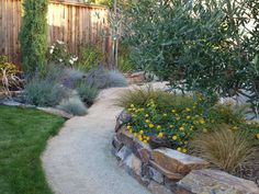 a garden with flowers and plants next to a wooden fence in the middle of it