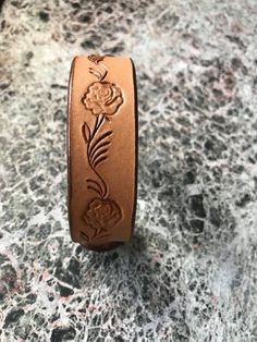 a close up of a leather bracelet on a marble surface with flowers and leaves engraved on it