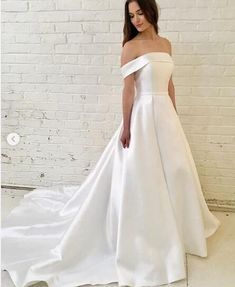 a woman in a white wedding dress standing against a brick wall with her hands on her hips