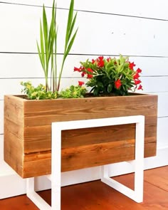 a wooden planter with red flowers in it on a white bench next to a wall