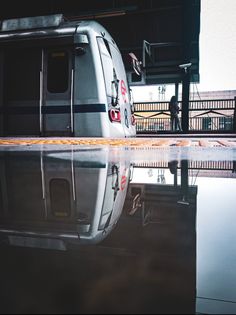 a silver train parked next to a loading platform with its reflection in the wet ground