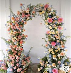 an arch made out of flowers and greenery with blue, pink, yellow and white flowers