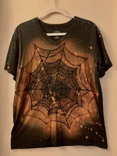 a t - shirt with a spider web design on the front and bottom, hanging from a hanger