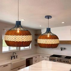 two lights hanging from the ceiling in a kitchen with white counter tops and cabinets below