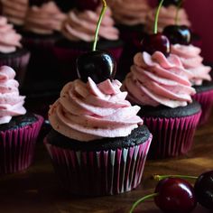 cupcakes with pink frosting and cherries on top sit on a table