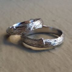 two silver rings sitting next to each other on top of a sand covered ground,