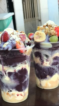 two cups filled with ice cream and fruit on top of a wooden table next to each other