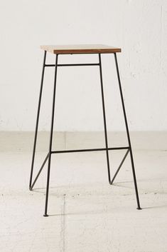 a black metal stool with a wooden seat and back rest in front of a white wall