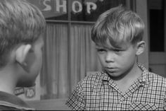 a young boy standing in front of a store talking to another child who is looking at him