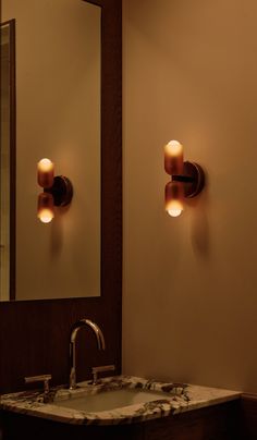 a bathroom sink sitting under a mirror next to a wall mounted faucet with two lights on it