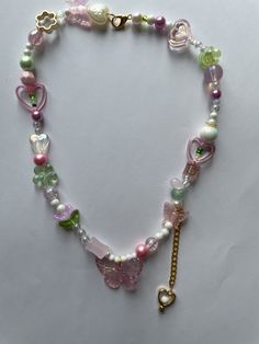 Embrace the whimsical charm of our Fairycore Butterfly Necklace! This handmade beaded necklace features a delightful mix of pink and green beads, adorned with butterflies, hearts, and flowers. Perfect for adding a touch of fairycore and kawaii style to any outfit, this necklace is a must-have for those who love unique and playful jewelry. Ideal for personal use or as a thoughtful gift, this necklace is designed to bring joy and enchantment to your accessory collection. The intricate beadwork and Pink Heart-shaped Beaded Necklaces, Cute Handmade Green Beaded Necklaces, Pink Kawaii Jewelry With Colorful Beads, Cute Butterfly Necklace For Gift, Pink Beaded Charm Necklaces With Round Beads, Pink Beaded Charm Necklace With Round Beads, Sweet Pink Jewelry With Colorful Beads, Pink Round Beads Kawaii Jewelry, Pink Handmade Fairy Kei Jewelry