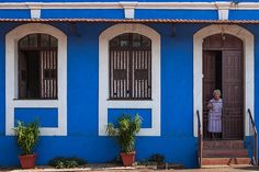 a woman standing in the doorway of a blue and white building with potted plants