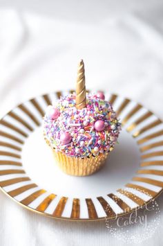 a cupcake topped with sprinkles and a single candle on a plate